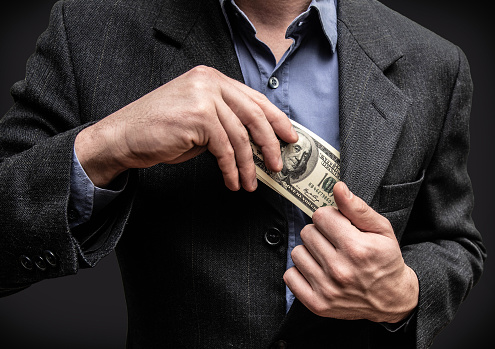 Man holding hundred dollar money in his pocket, close-up of his hands and money. Serious businessman, buying goods, giving bribes, corruption.
