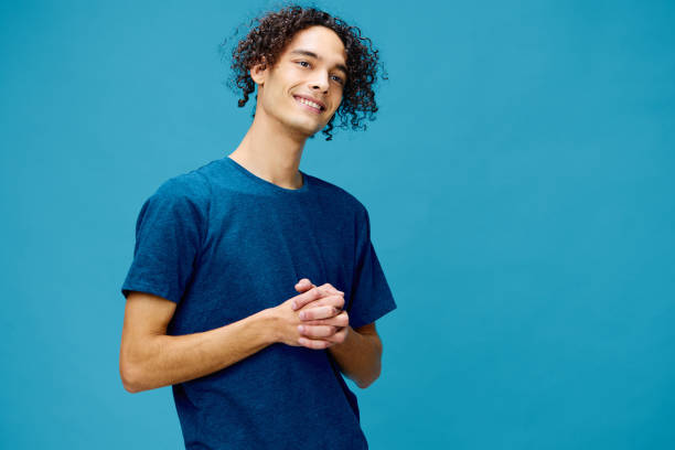 istock Smiling joyful cute curly tanned Caucasian guy in basic t-shirt posing isolated on over blue background. Lifestyle and Emotions concept. Good offer with copy space for ad 2147725379