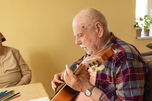 Group therapy session at a nursing home featuring an older man playing soothing melodies on his guitar.