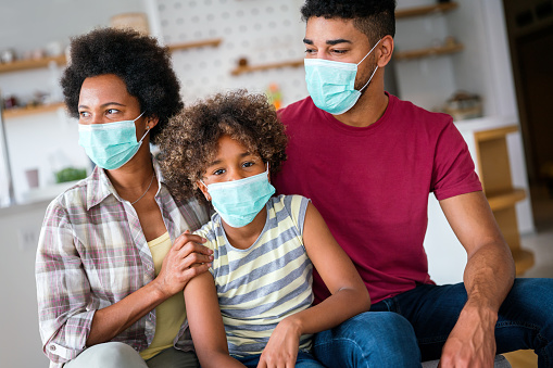 Young african american family in medical masks during home quarantine. Family is wearing facemasks during coronavirus and flu outbreak. Virus and illness protection, COVID