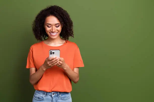 Photo of Photo of cute good mood lady dressed orange t-shirt communicating apple iphone samsung device empty space isolated khaki color background