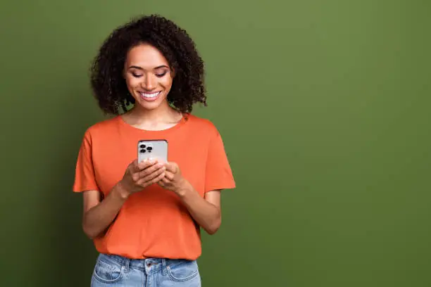 Photo of cute good mood lady dressed orange t-shirt communicating apple iphone samsung device empty space isolated khaki color background.