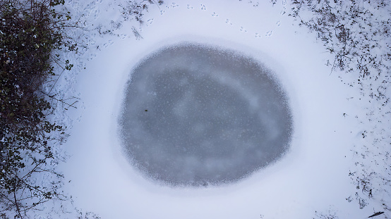 Frozen lake with snow and trees captured with drone