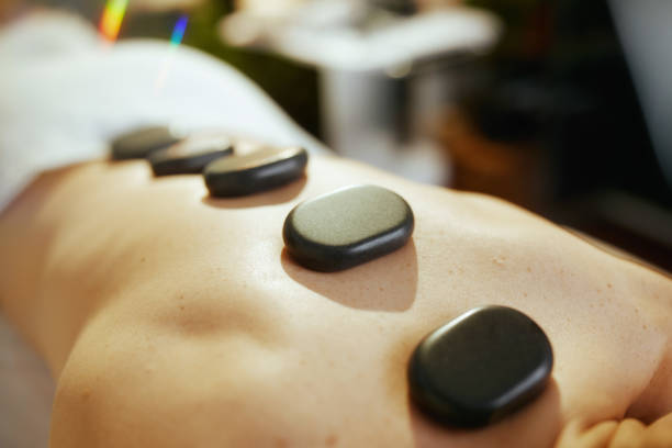 Healthcare time. Closeup on relaxed woman in massage cabinet having hot stone massage and laying on massage table.