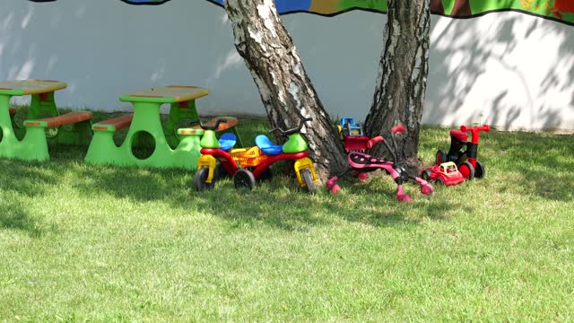 Riding toys, trucks plastic picnic tables under tree under tree outside primary school.