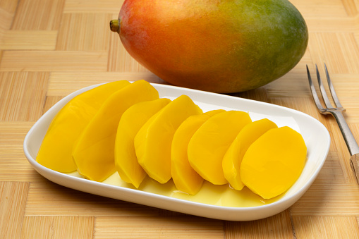 Plate with pickled mango slices and a fresh whole mango in the background