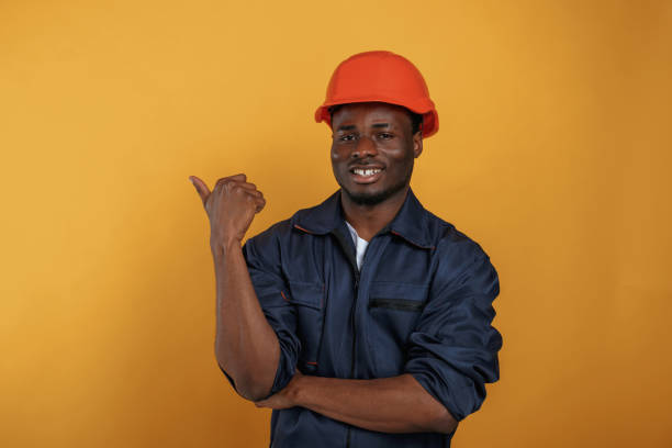 istock Guy in hard hat showing copy space by finger. Handsome black man is in the studio against yellow background 2148029526