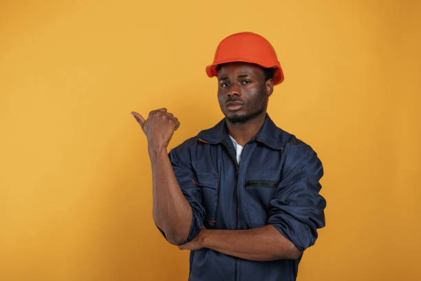 istock Guy in hard hat showing copy space by finger. Handsome black man is in the studio against yellow background 2148029540