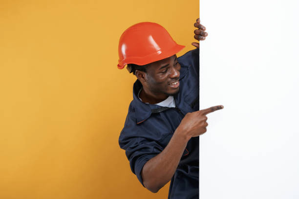 istock Engineer in hard hat is hiding behind white copy space. Handsome black man is in the studio against yellow background 2148029555