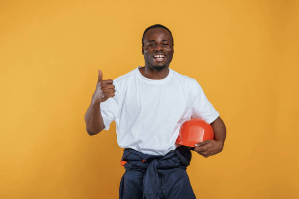 istock Holding hard hat in hand. Handsome black man is in the studio against yellow background 2148029581