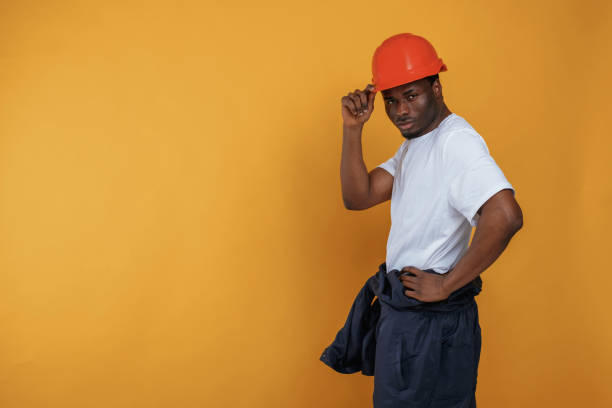 istock Standing and posing, construction worker in hard hat. Handsome black man is in the studio against yellow background 2148029631
