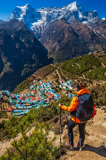 Young woman, wearing red jacket, is standing on the top of a rock and looking at Namche Bazaar village in Mount Everest National Park. This is the highest national park in the world, with the entire park located above 3,000 m ( 9,700 ft). This park includes three peaks higher than 8,000 m, including Mt Everest. Therefore, most of the park area is very rugged and steep, with its terrain cut by deep rivers and glaciers.