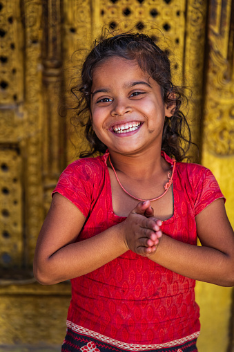 Little Nepali girl saying namaste in Bhaktapur. Bhaktapur is an ancient town in the Kathmandu Valley and is listed as a World Heritage Site by UNESCO for its rich culture, temples, and wood, metal and stone artwork.