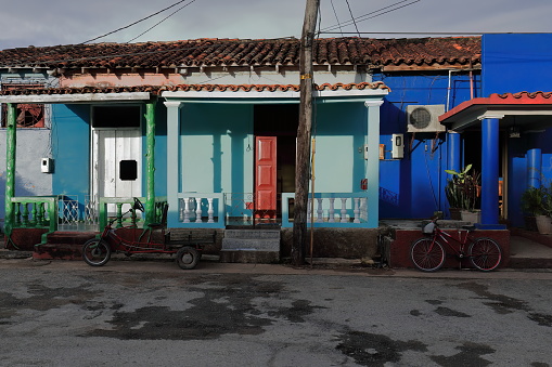 Viñales, Cuba-October 9, 2019: Sunny porches of one-storey vernacular houses facing the setting sun, colorfully painted with open doors and bicycle-tricycle parked outside, on Calle Adela Azcuy Street