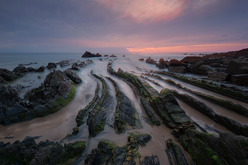 Flysch of Barrika beach, Bizkaia, at sunset with a dramatic sky of warm colors and the tide water entering between the rocks