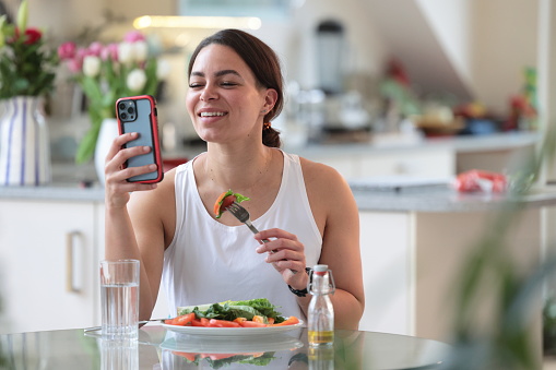 Multiracial woman uses phone while eating salad at home