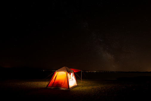 A camping tent glows under a night sky full of stars. Outdoor Camping adventure