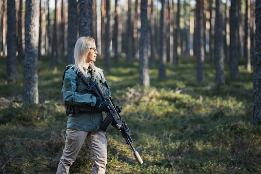 Beautiful army girl with a modern AK 12 suppressed rifle in the forest at war. Close up photo