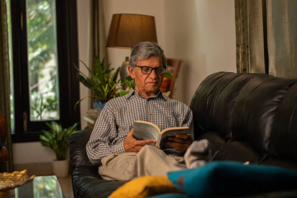 istock Senior man reading book on comfortable sofa at home 2148040438