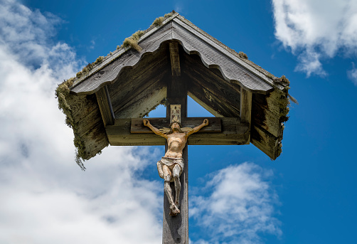 Wooden christian wayside cross with jesus christ figurine agaisnt blue sky