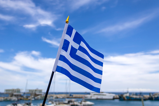 Greek national flag fluttering in the wind at sea harbor