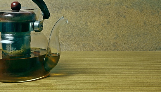 Transparent glass teapot half filled with tea.