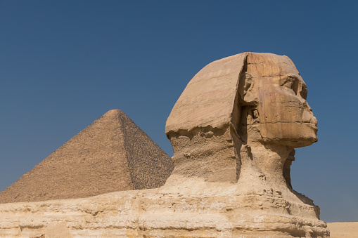 Sphinx of Giza in profile with the Great Pyramid of Kheops in Egypt, blue sky.  Copy space