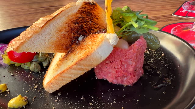 Tasty beef steak tartare with toast bread and a pickle on a plate, raw meat dish, 4K shot