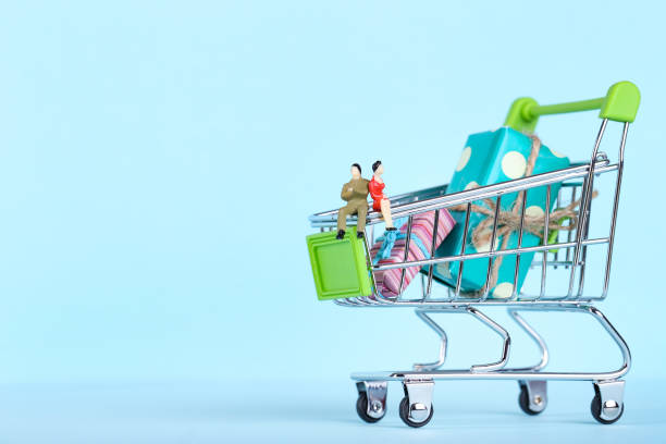 Miniature people with shopping cart and gift boxes on blue background