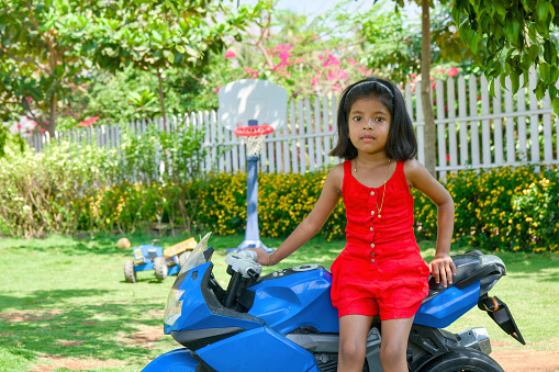A charming image of a young girl with a vibrant red dress sitting playfully on a classic blue motorbike