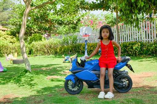 A charming image of a young girl with a vibrant red dress sitting playfully on a classic blue motorbike