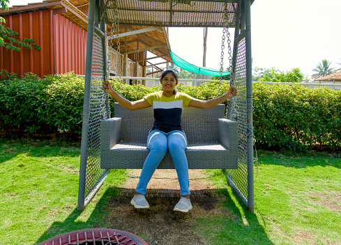 A serene image of a young woman relaxing on a swing in a beautiful home garden