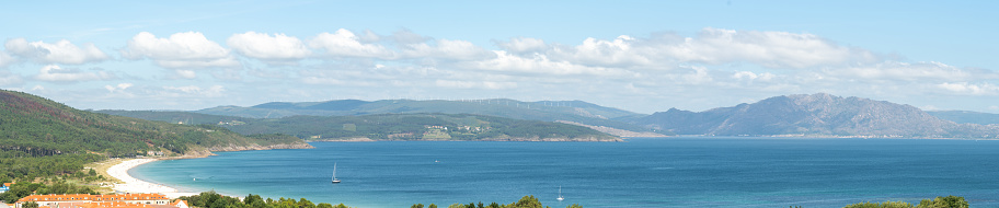 Panoramic view of Enseada da Langosteira (Finisterre), with windmills in the background and a sky full of clouds. A sunny day in Galicia.