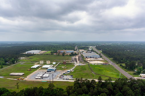 Aerial view of Industry in Southeastern Texas with Manufacturing, Fuel storage and a Railroad station along a two lane highway with traffic under an overcast stormy sky.