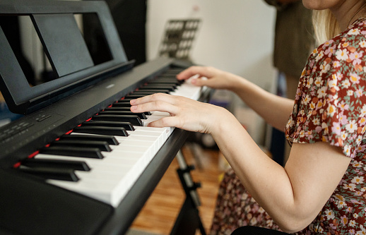 Close-up of a young woman playing a keyboard while making music in a small recording studio at home
