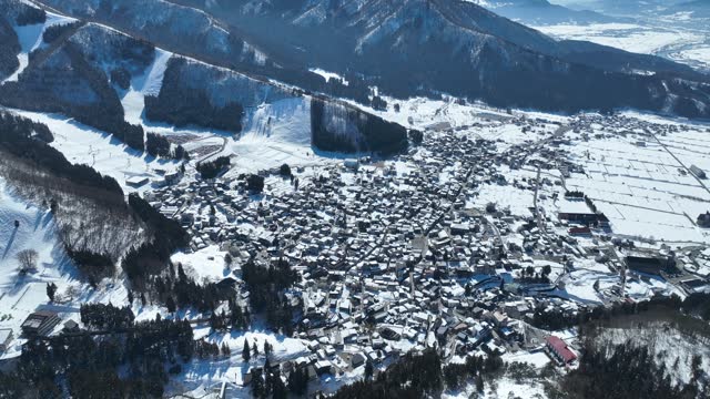 Aerial establishing shot of Japans Nozawaonsen Mountain Ski Resort Village. Camera slowly ascends and pans down revealing the mountain village resort. Clear Winter Day