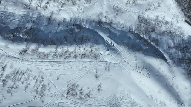 Father and Son Walk through thick snowy mountain side. Top down aerial shot looking down from above as the pair hike along he snowy covered mountain. Japan Nozawaonsen Mountains, clear winter day