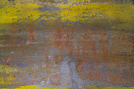 Close up dirty painted yellow and rust color concrete wall with black smudges of black and grey dirt and mildew. Background texture