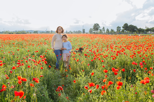 woman and her child standing in the poppy field next to their running dog on a sunny day