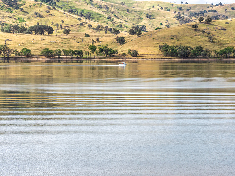Fishing boat leaving wake on Lake Hume and the rolling hills at Tallangatta, Victorian High Country