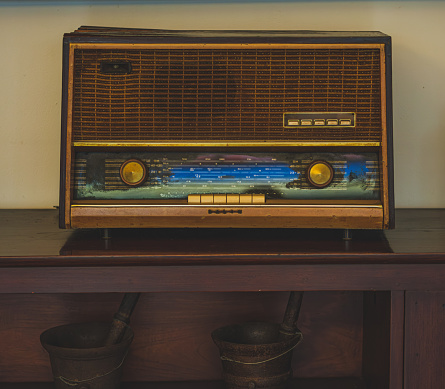 A classic, art deco style radio sits on a rustic wooden shelf. The radio is in good condition with a polished wood cabinet and a metal tuner.