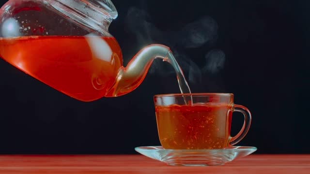Herbal tea being poured from a cup into a glass, contrasted against a dark backdrop, illustrating the cultural ritual and hospitality of tea serving. HDR, 4K.