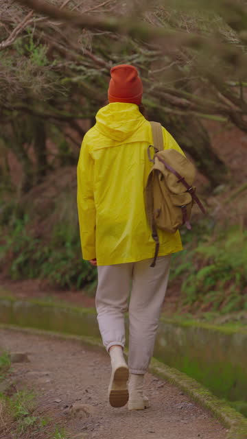 A girl in a yellow jacket travels with a backpack and visits extraordinary places and trails on the island of Madeira, Levada dos Tornos, Portugal. Vertical video