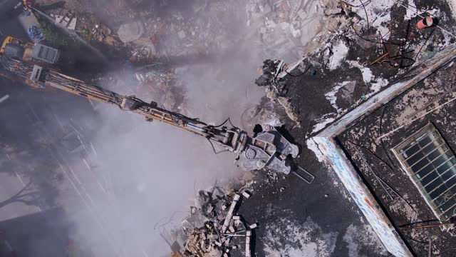 Old Building Demolition By An Excavator With Crusher Attachment. - aerial shot