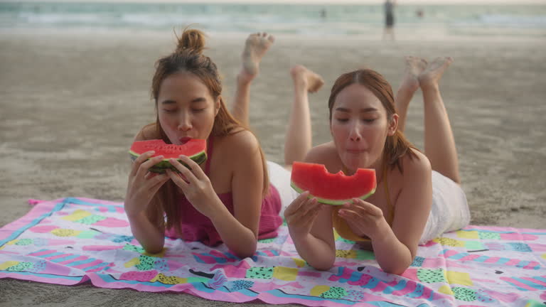 Two beautiful young friends having fun eating watermelon on the beach at sunset.