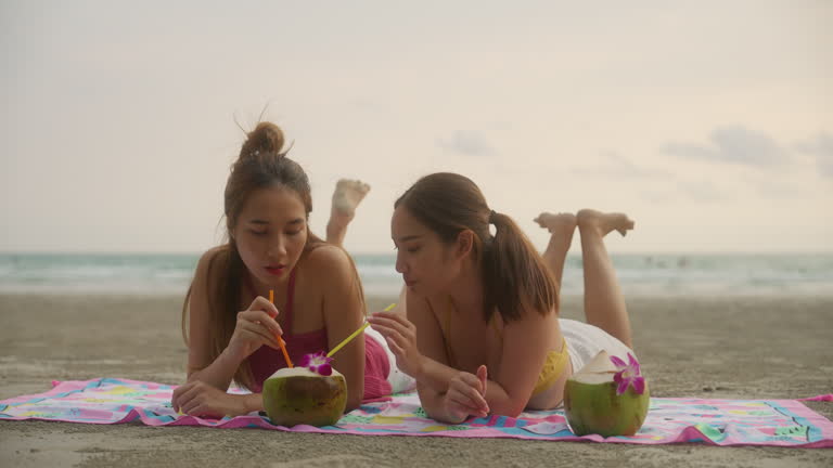 Two beautiful young friends having fun eating watermelon and coconut on the beach at sunset.