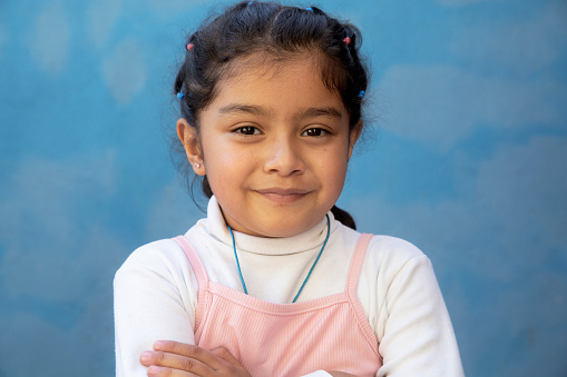 A portrait of a young girl with her arms folded in front of a blue wall