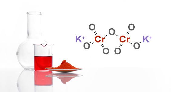 Potassium Dichromate in chemical watch glass place next to red liquid in beaker and Flat Bottom Flask. The structure of a chemical compound is shown on the side.