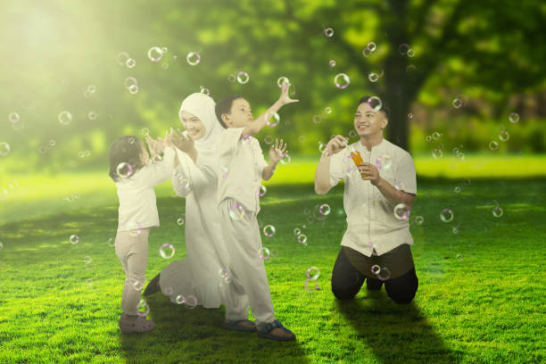 Young parents playing soap bubbles with their children at park enjoying spring or summer