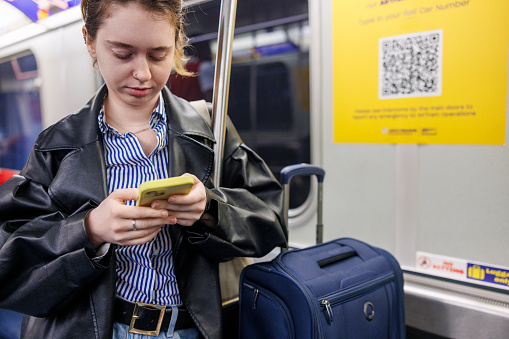 Young Caucasian businesswoman on a train, engaging with her smartphone. Woman managing work-related communications and organizing her schedule on business trip